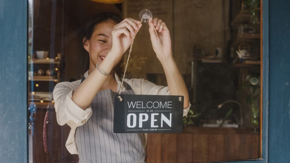 young-manager-girl-changing-sign-from-closed-open-sign-door-cafe-looking-outside-waiting-clients-after-lockdown